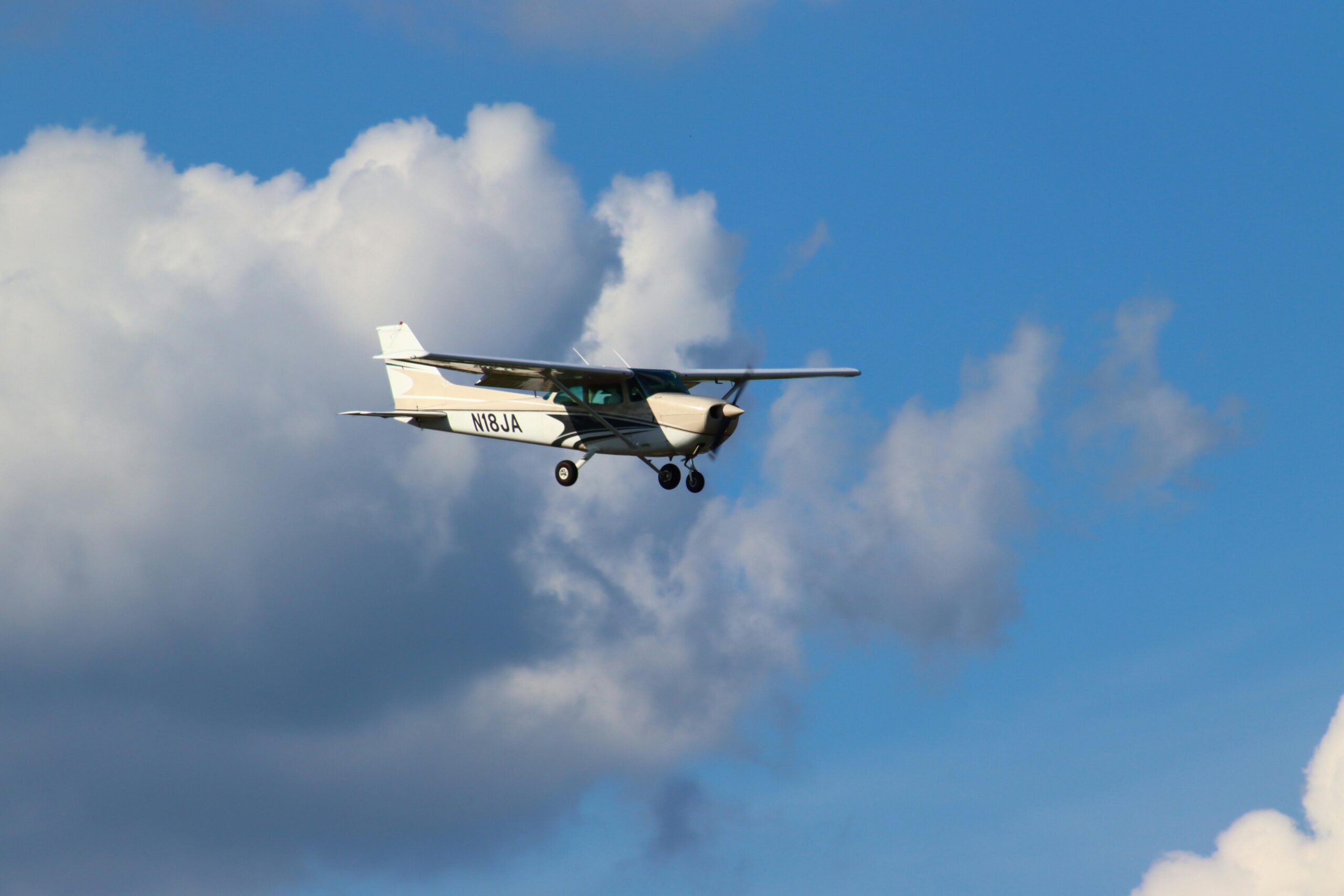 A small aircraft flying among white clouds in a clear blue sky.